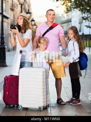 Allegro positivo famiglia turistiche usando la mappa e prendendo foto della città passeggiando con telecamera e telefono Foto Stock