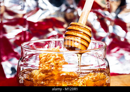 Il miele fresco il vaso e dipper stick su una tavola di legno con erba - miele di gocciolamento Foto Stock