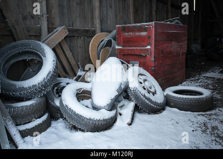 Pila di vecchi pneumatici per auto coperto di neve nel vecchio garage in legno Foto Stock