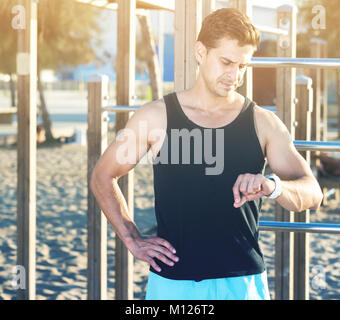 Montare fisicamente un uomo guarda smartwatch sulla terra di sport sulla spiaggia Foto Stock