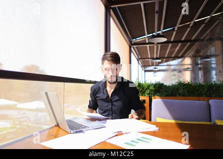 Lavoratore di ufficio ordinamento di carte sul tavolo vicino al computer portatile. Foto Stock