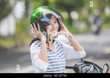 Donna felice il fissaggio il suo casco in moto nella strada di città Foto Stock