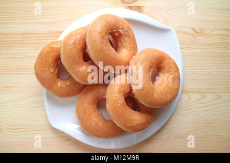Vista dall'alto di zucchero-ciambelle vetrato servita su piastra bianca sul tavolo di legno Foto Stock