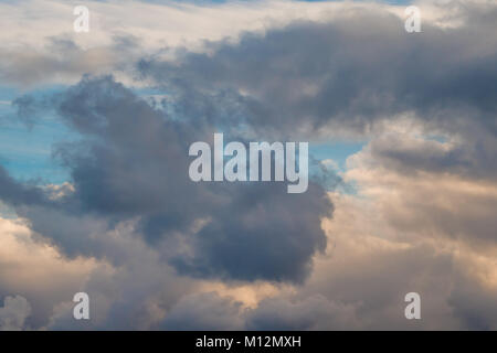 Un ciuffo di nuvole scure circondato da soffici nuvole contro un cielo blu e giallo sole del mattino Foto Stock