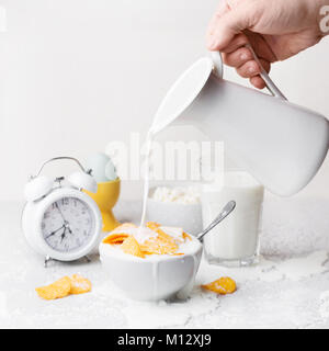 Man mano versando il latte bianco ciotola con il mucchio di dorate e croccanti patatine su sfondo bianco, copia dello spazio. Cibo malsano concetto Foto Stock