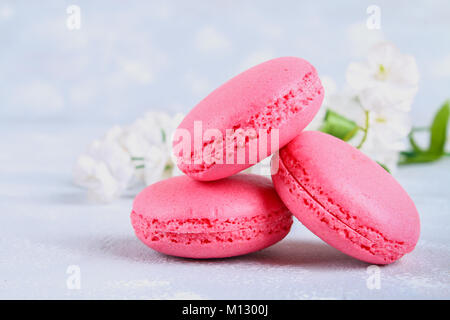 Rosa e viola gli amaretti sul grigio di un tavolo circondato da fiori rosa e bianchi Foto Stock