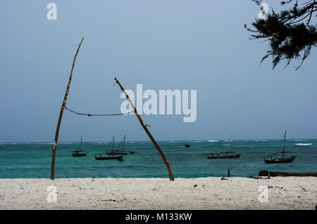 Due poli legati insieme con una corda, forse un inpromptu linea di lavaggio, con un tradizionale dhow barche in background sulla spiaggia di Nungwi Zanzibar Foto Stock