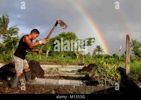 Famer coltivare il suo terreno agricolo mentre la Mt. Mayon eruttate (arcobaleno sul lato destro) nelle prime ore del mattino con ceneri vulcaniche cade dal punto di vista di Cagsawa Parco Nazionale in Daraga, Albay, Bicol a gennaio 26, 2018. L'Istituto filippino di vulcanologia e sismologia (PHILVOLCS) dichiarati numero di avviso 8 e una più ampia della zona di pericolo a 8 chilometri dopo le esplosioni la continua attività attive del vulcano di questo passato diversi giorni. Secondo i rapporti è un totale di 74.000 persone sono colpite e 100 milioni di euro di danni nei terreni agricoli conformemente al Dipartimento di Agricoltura ( Foto Stock