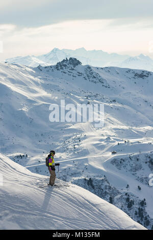 Un maschio di sciatore sorge e si ammira la vista con le montagne e la ski area Tre Valli di distanza, Méribel, Francia Foto Stock