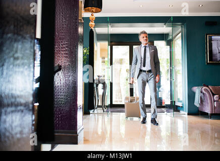 Imprenditore maturo entrando in hotel con i bagagli. Foto Stock