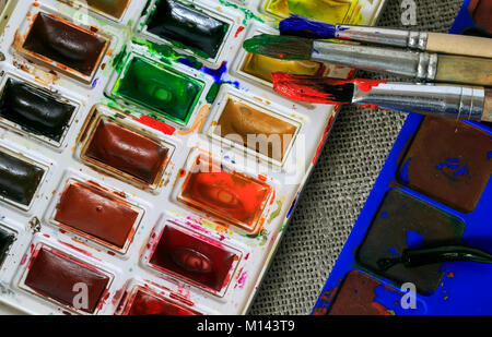 Background artistico dello Studio spazzole sono tutti macchiati con colori giacciono su una serie di acquerelli luminosi sulla tela in tessuto Foto Stock