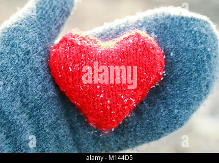 Maglia caldo cuore rosso è coperto con il freddo dei cristalli di ghiaccio si appoggia nel palmo in grigio i guanti Foto Stock
