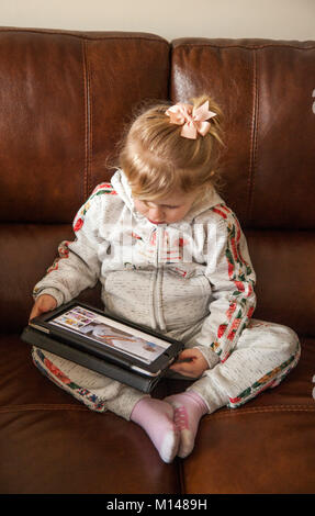 Due anni di ragazza seduta su un divano orologi vignette su un iPad Foto Stock