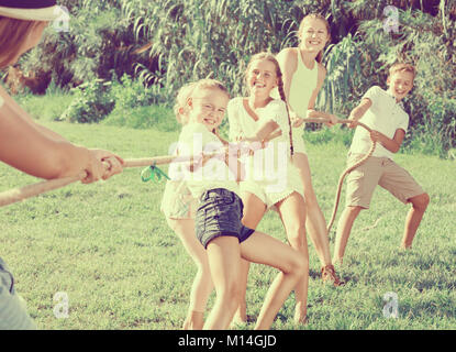 I bambini con mamma e papà la riproduzione di tiro della fune durante il comune di giochi all'aperto sulla giornata di sole Foto Stock