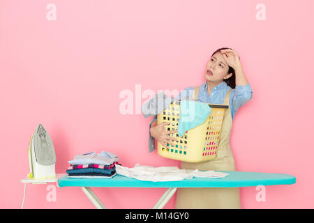 Piuttosto elegante houseworker femmina sensazione di stanchezza e ottenere il mal di testa doloroso quando ella tenendo un cesto della biancheria preparazione alla stiratura di capi di abbigliamento isolati su Foto Stock