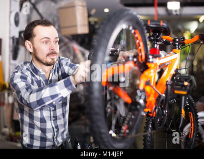 Giovane uomo in grembiule andando a montare la ruota di bicicletta in moto officina Foto Stock