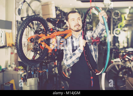 Positivo l'uomo europeo Nel grembiule considerando la composizione della ruota per bicicletta Foto Stock