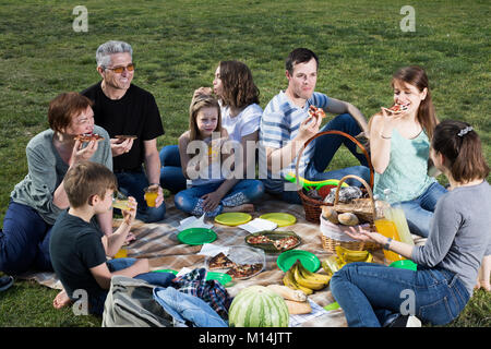 La famiglia felice con i bambini a parlare e mangiare la pizza a picnic nel parco Foto Stock