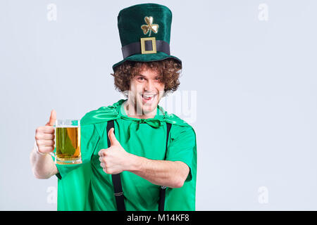 Un giovane curly-dai capelli uomo in tuta di San Patrizio con una tazza o Foto Stock