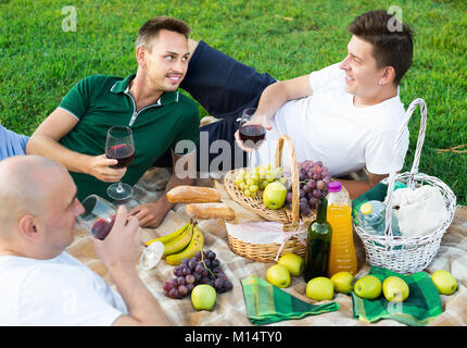 Tre uomini amici godendo la vita sulla picnic all'aperto in compagnia maschile Foto Stock