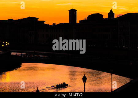 Silhouette di Pisa - tramonto sulla città di Pisa oltre il fiume Arno durante la notte mentre una squadra di canottaggio riga al di sotto di un ponte Foto Stock