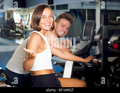 Giovane uomo sorridente e la donna in fase di riscaldamento prima di allenamento ciclismo utilizzando macchine cardio Foto Stock