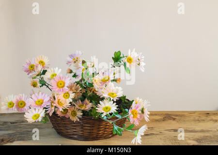 Profumo di rosa pallido crisantemi in un cesto di vimini su un tavolo di legno su uno sfondo luminoso Foto Stock