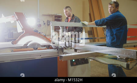 Lavoratori carpentieri sono il taglio di legno sulla scheda sega elettrica alla fabbrica di mobili Foto Stock