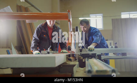 Lavoratori carpentieri sono il taglio di legno sulla scheda sega elettrica alla fabbrica di mobili Foto Stock