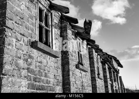 Foto in bianco e nero di un vecchio edificio in mattoni con finestre rotte Foto Stock