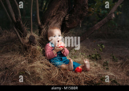 Bambina seduto sotto un albero e si mangia un apple. Foto Stock