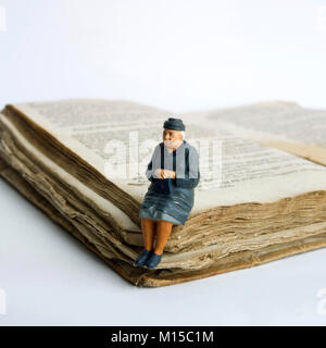 Signora anziana, figurine in miniatura, seduto su un vecchio libro Foto Stock