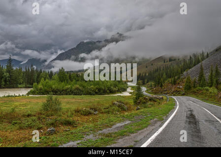 Vista panoramica con un avvolgimento umido strada asfaltata in montagna, nebbia, la foresta e il fiume in tempo nuvoloso Foto Stock