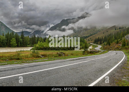 Vista panoramica con un avvolgimento umido strada asfaltata in montagna, nebbia, la foresta e il fiume in tempo nuvoloso Foto Stock