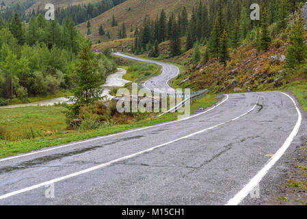 Vista panoramica con un avvolgimento umido strada asfaltata in montagna, nebbia, la foresta e il fiume in tempo nuvoloso Foto Stock