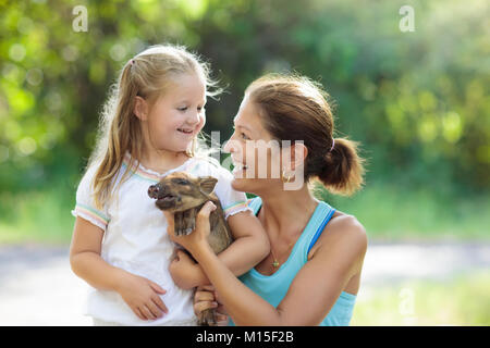 Bambini a giocare con gli animali della fattoria. Bambino alimentazione di animale domestico. Giovane madre e bambina tenendo il cinghiale baby al giardino zoologico. Kid giocando con newbo Foto Stock