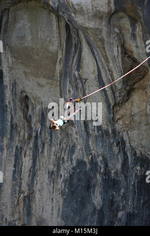 Ragazza giovane bungee jumper appeso a una fune, le rocce scure della grotta Prohodna visto a sfondo Foto Stock