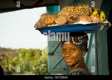 Una donna africana porta una varietà di frutta e noci in una ciotola che porta sulla sua testa. Foto Stock