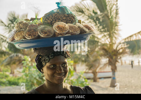 Una donna africana porta una varietà di frutta e noci in una ciotola che porta sulla sua testa. Foto Stock