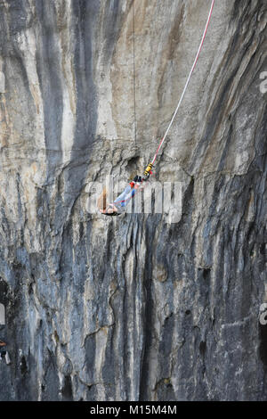 Ragazza giovane bungee jumper appeso a una fune, le rocce scure della grotta Prohodna visto a sfondo Foto Stock