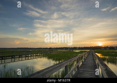 Lunga passerella in legno pier su marsh ad alta marea con un fantastico del cielo della sera e al tramonto Foto Stock