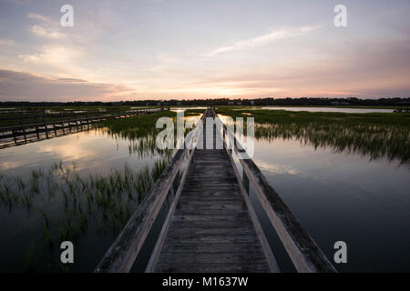 Lunga passerella in legno pier su marsh ad alta marea con un fantastico del cielo della sera e al tramonto Foto Stock