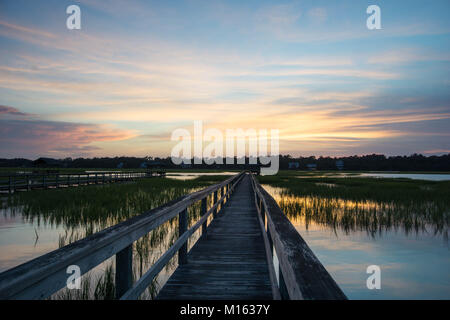 Lunga passerella in legno pier su marsh ad alta marea con un fantastico del cielo della sera e al tramonto Foto Stock