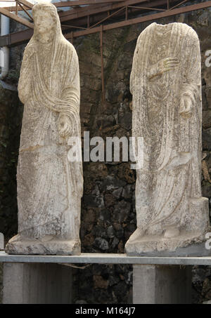 Abbandonata e parzialmente erosa statue di una donna in un mantello con il velo che copre la testa e una testa di statua in Porta Nocera nell'antica città di Foto Stock