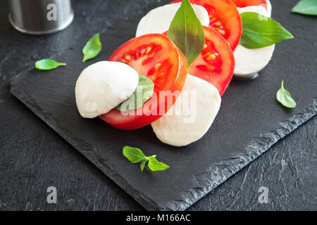 Tradizionale Italiano insalata caprese - fette di pomodoro, mozzarella e basilico in pietra scura, sfondo vicino. Insalata caprese, italiano mediterran Foto Stock