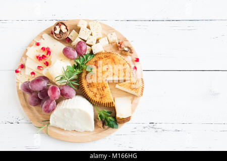 Un vassoio di formaggi con formaggi assortiti, uva, dadi bianco su sfondo di legno, copia dello spazio. Formaggi italiani e piatti di frutta. Foto Stock