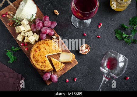 Un vassoio di formaggi con formaggi assortiti, uva, i dadi su sfondo nero, copia dello spazio. Formaggi italiani e piatti di frutta con miele e vino. Foto Stock