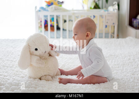 Little baby boy, bimbo, gioca in casa con il giocattolo di peluche nel letto in camera da letto Foto Stock