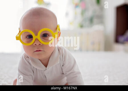 Little baby boy, bimbo, giocando a casa con strani occhiali in letto matrimoniale in camera da letto Foto Stock