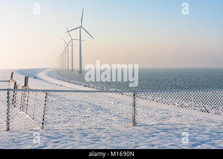 Dicco olandese in inverno con neve, recinzione e turbine eoliche Foto Stock